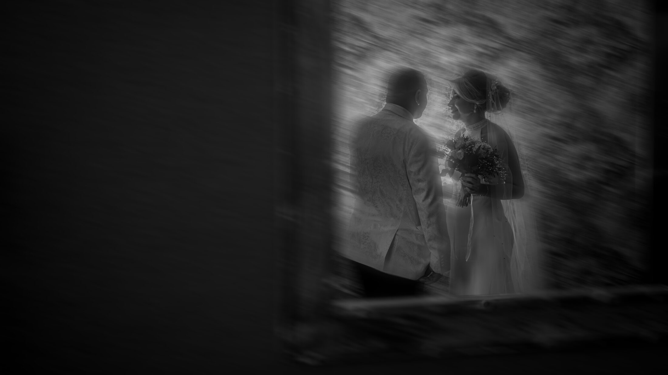 Silueta de los novios en blanco y negro, enmarcados por un arco entre destellos de luz difuminados