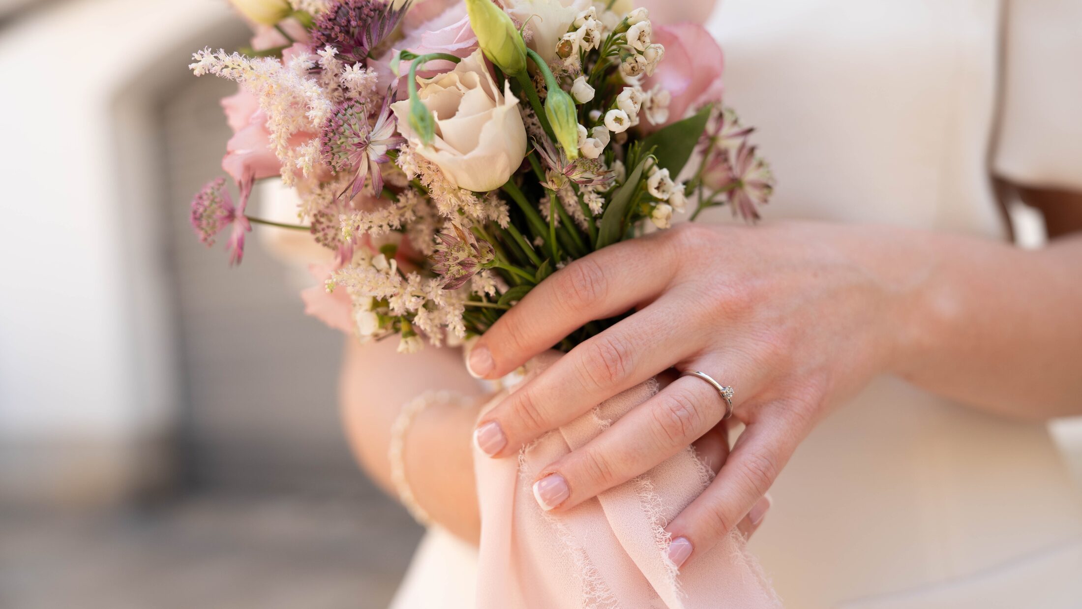 Detalle de un ramo de novia y un anillo de compromiso entre los dedos