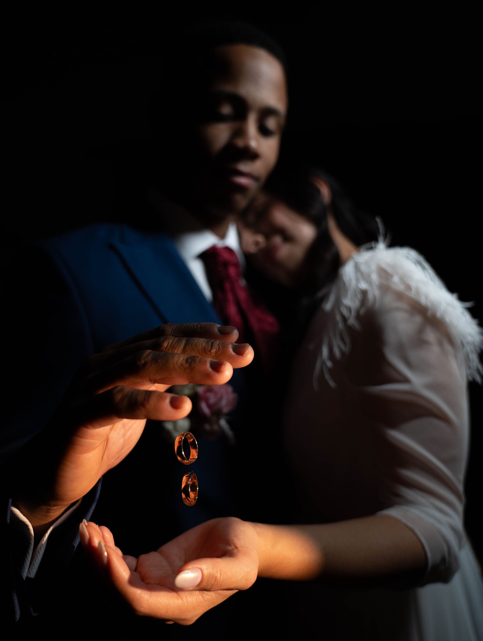 Alianzas cayendo entre las manos de los novios, con la pareja desenfocada al fondo